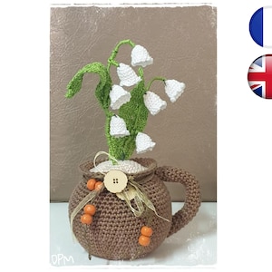 May include: A crocheted lily of the valley bouquet in a brown crocheted pot with a handle. The pot has orange beads and a wooden button.
