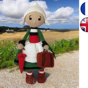 Peut inclure: Une poupée en crochet vêtue d'un costume traditionnel néerlandais, tenant un parapluie rouge et une valise brune. La poupée porte un bonnet blanc, une robe verte et noire et un corsage à rayures rouges et noires.
