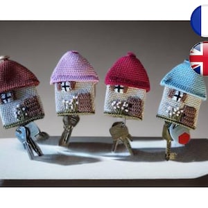 May include: Four miniature crocheted houses in pink, red, blue, and brown, each with a key attached, standing on a white surface.