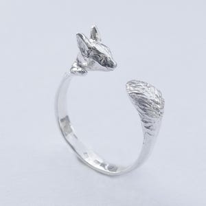 May include: A silver ring with a detailed fox head design. The fox's tail wraps around the ring band.