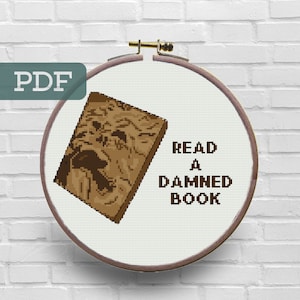 May include: A brown and white cross-stitch embroidery hoop with a brown book and the text "READ A DAMNED BOOK".