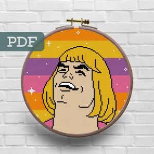 May include: A cross-stitch pattern of a pixelated image of He-Man from the Masters of the Universe cartoon. He-Man is depicted with a surprised expression and his signature blonde hair. The background is a rainbow gradient with white stars.