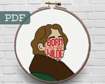 May include: A cross-stitch pattern featuring a portrait of a person with brown hair and a green and brown outfit. The text "BORN TO BE WILDE" is stitched across the person's face in red.