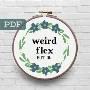 Puede incluir: Un aro de bordado blanco con una corona de flores verdes y azules alrededor del texto "weird flex but ok".