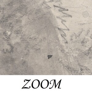 May include: A close-up of a textured, gray surface with a black triangle shape in the center. The surface has a rough, uneven texture, and there are faint lines and markings visible.