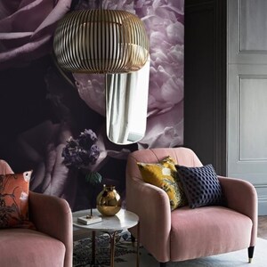 Puede incluir: Dos sillones de terciopelo rosa con almohadas, una mesa auxiliar redonda de m&aacute;rmol blanco con patas doradas y un jarr&oacute;n dorado sobre la mesa. Los sillones est&aacute;n frente a una pared con un papel tapiz floral con grandes peon&iacute;as y rosas rosas.