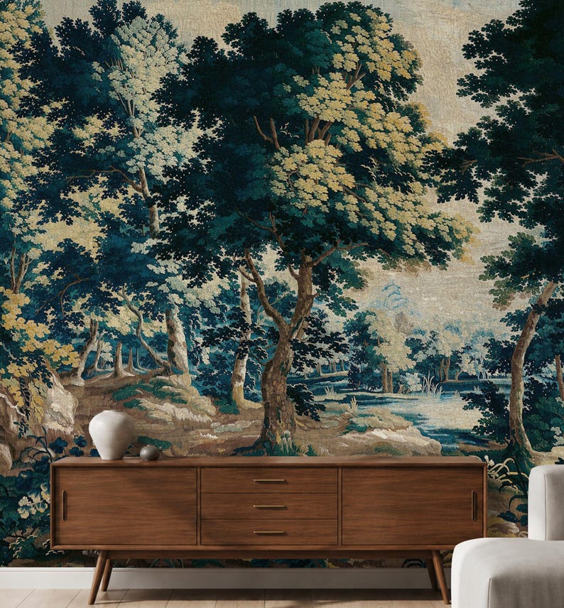 European antique tapestry wallpaper in rich deep blue, green, and warm earthy tones, featuring mature trees, lush woodland foliage and a tranquil pond, styled with a mid-century wooden sideboard, sculptural ceramics, and soft neutral seating. The exquisite, timeless elegance of 17th-century Verdure style blends classical artistry with handcrafted warmth to bring historical beauty and natural poetry into your home, for those who want to elevate their interiors with refined heritage character.