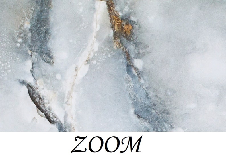 May include: Close-up of a light blue and gray marble texture with white and gold veins. The marble has a cloudy, ethereal appearance.