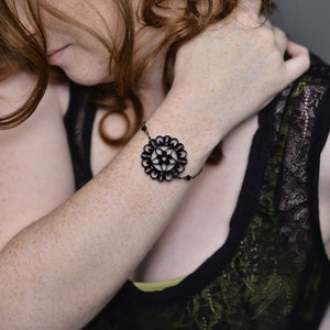 Pode incluir: Uma mulher vestindo um top de renda preta com uma pulseira preta e prateada com um design floral.
