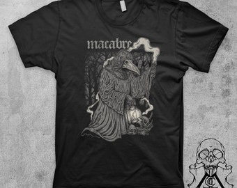 May include: Black t-shirt with a graphic of a hooded figure with a long beak, holding a lantern in a dark forest. The text "macabre" is printed above the figure.