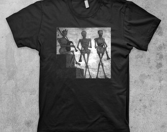 May include: Black t-shirt with a graphic print of three skeletons playing musical instruments. The skeletons are wearing crowns and holding a drum, a clarinet, and a flute.