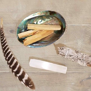 May include: A collection of smudging tools including a white sage bundle, palo santo sticks in a seashell, and a clear quartz crystal.