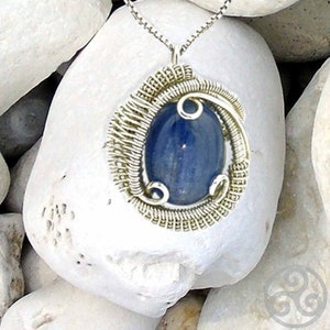 May include: A silver wire wrapped pendant featuring a blue gemstone. The pendant is hanging from a silver chain.