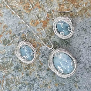 May include: A silver wire wrapped aquamarine pendant necklace and matching earrings set. The aquamarine stones are oval shaped and have a light blue color.