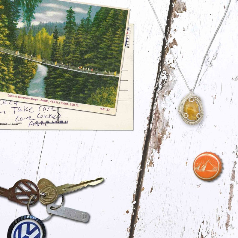 May include: A vintage postcard with a photo of a suspension bridge over a river in a forest. The postcard has handwritten text that says "Take care, Love CUICKIC, All". There is a silver necklace with a yellow stone pendant, a bottle cap with a mountain design, and a set of keys with a Volkswagen logo keychain.