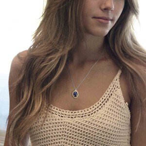 May include: A woman wearing a crocheted top with a silver chain necklace featuring a blue and gold pendant.