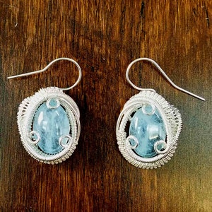 May include: A pair of silver wire wrapped earrings with light blue aquamarine stones.