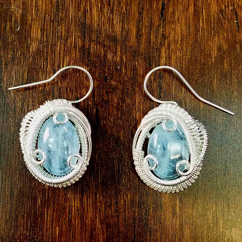 May include: A pair of silver wire wrapped earrings with light blue aquamarine stones.