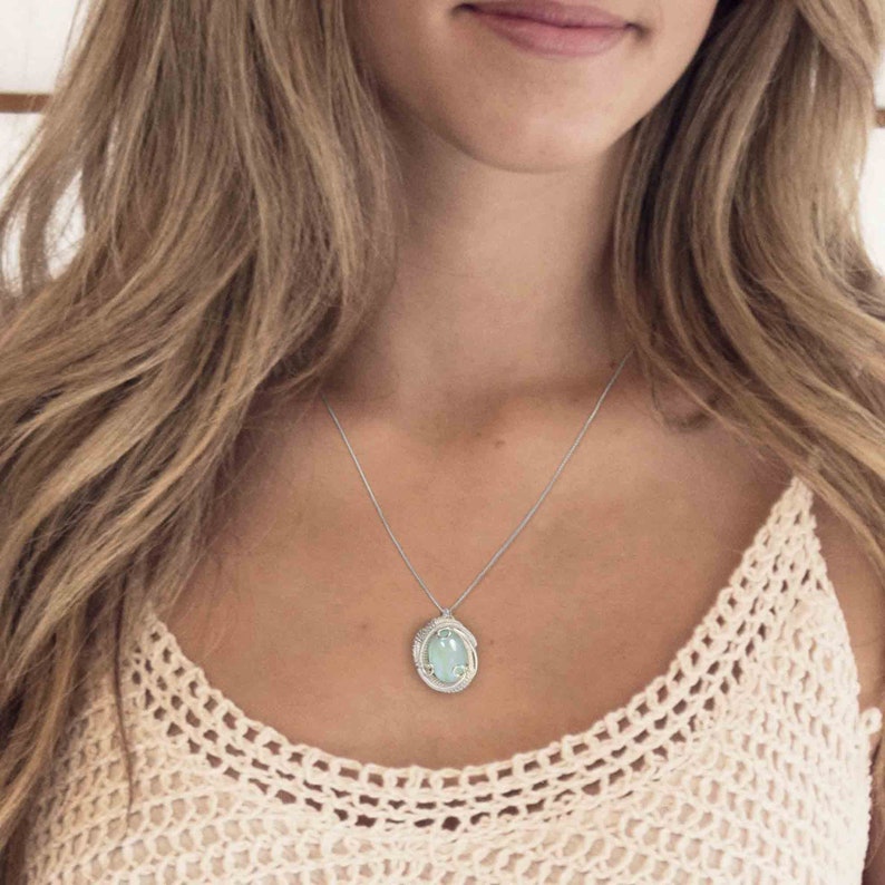 May include: A silver chain necklace with a light blue oval pendant. The pendant is set in a silver frame with a delicate design.