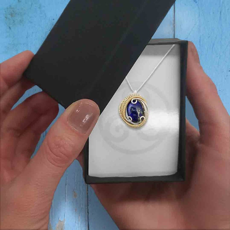May include: A blue gemstone pendant with gold and silver wire wrapping, in a black and white gift box.