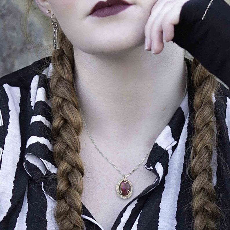 May include: A silver chain necklace with a pendant featuring a red oval gemstone surrounded by a gold wire design.