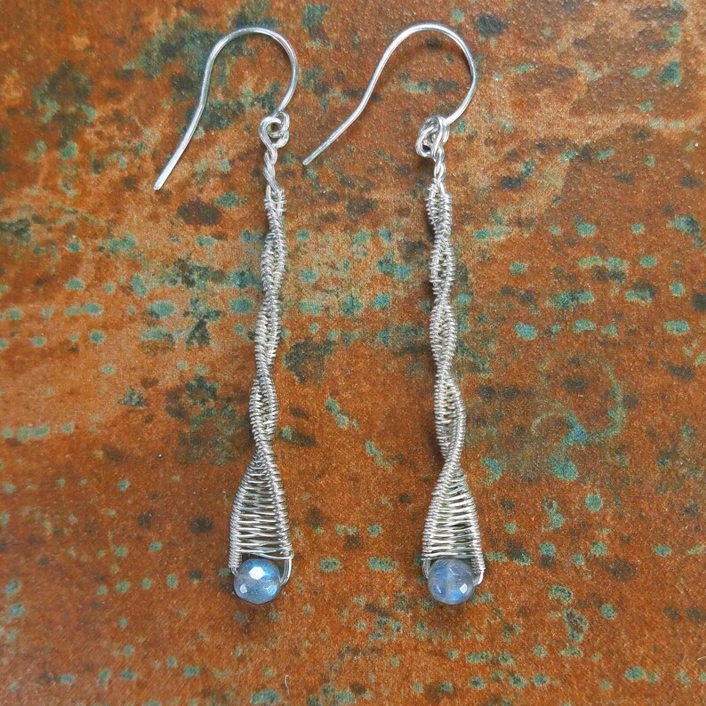 May include: Silver wire earrings with a blue gemstone at the bottom of each earring.