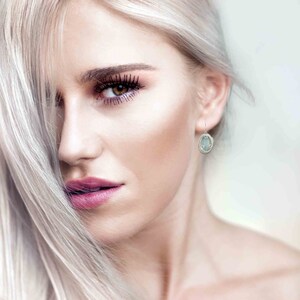 May include: A woman with long, platinum blonde hair wearing a pair of silver earrings with a light blue oval-shaped stone.