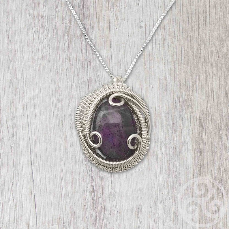 May include: A silver wire wrapped pendant featuring a purple gemstone. The pendant hangs from a silver chain.