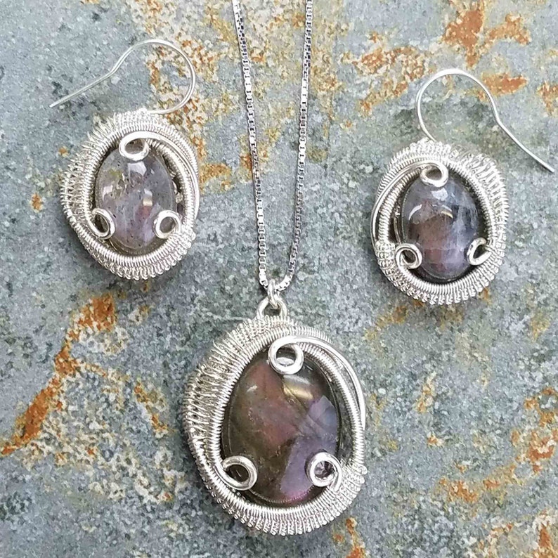 May include: A silver wire wrapped pendant necklace and matching earrings set with a purple and grey iridescent stone.