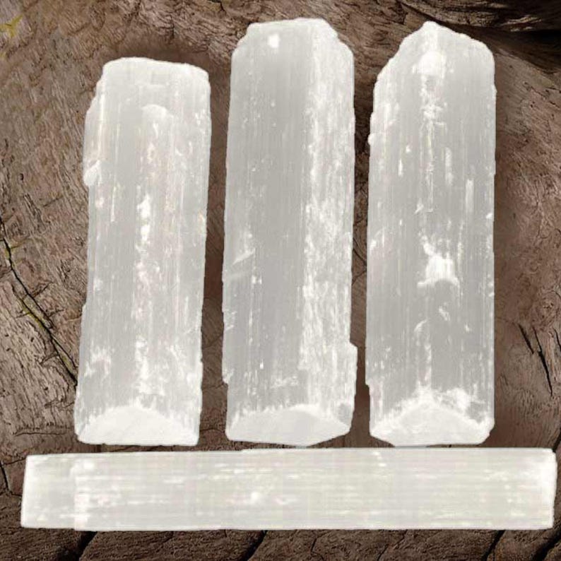 May include: Four white selenite wands, three standing upright and one lying horizontally. The wands are smooth and have a natural, crystalline texture.