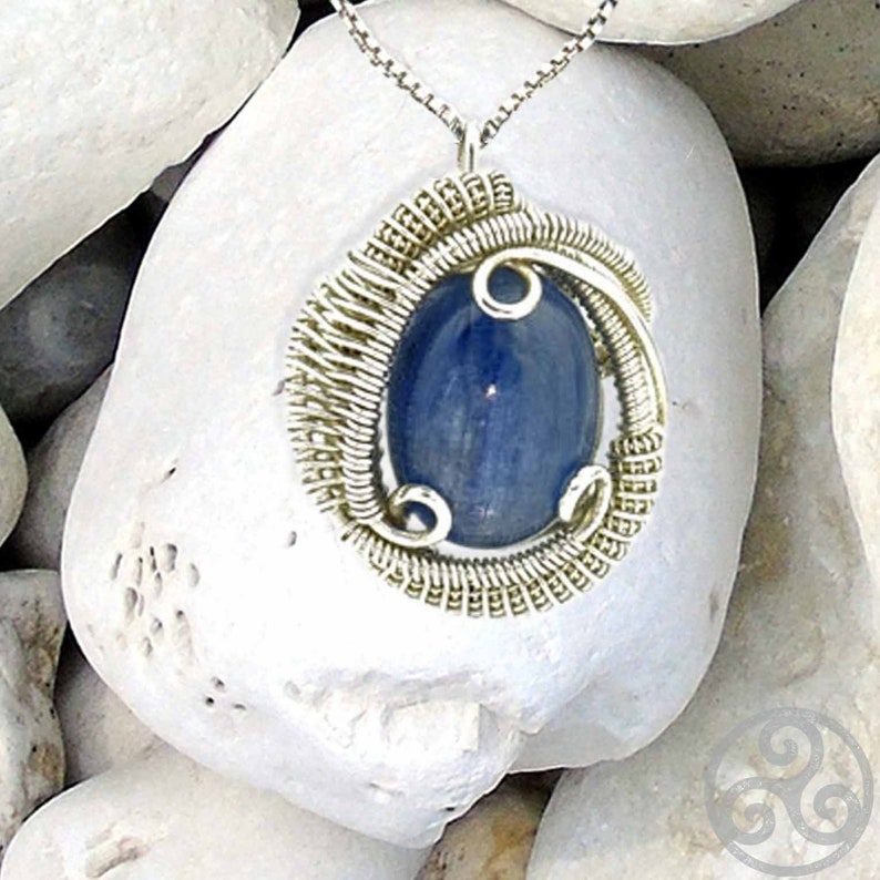 May include: A silver wire wrapped pendant featuring a blue gemstone. The pendant is hanging from a silver chain.