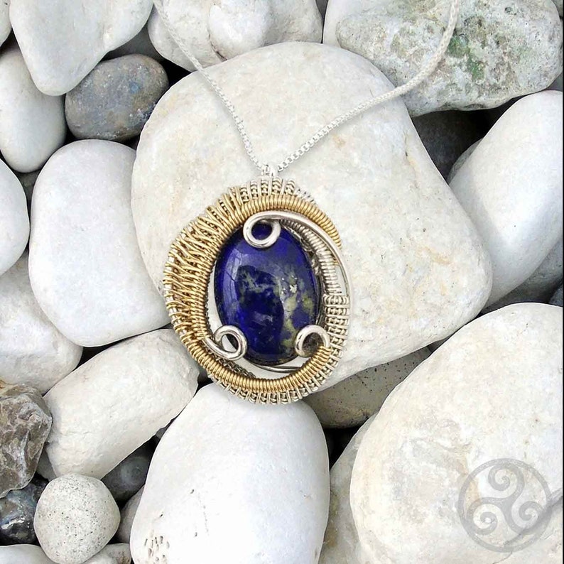 May include: A silver chain necklace with a pendant featuring a blue lapis lazuli stone set in a gold and silver wire wrapped design.