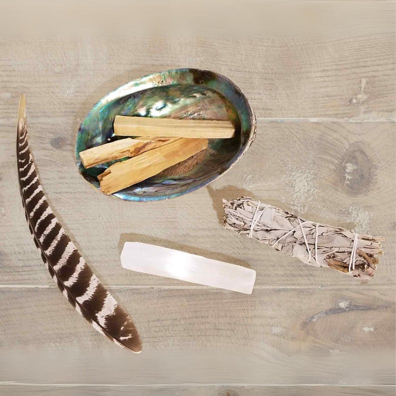May include: A collection of smudging tools including a white sage bundle, palo santo sticks in an abalone shell, and a clear quartz crystal.