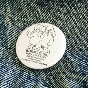 Puede incluir: Un botón blanco con una ilustración en blanco y negro de dos gatos. El texto en el botón dice "BORN TO DIE WORLD IS A FUCK I am trash man 410.757.864.530 DEAD COPS".
