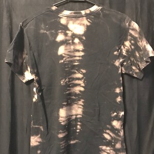 Puede incluir: Camiseta negra con un dise&ntilde;o salpicado de lej&iacute;a. La camiseta tiene cuello redondo y mangas cortas. El texto "ACIDDRIP CLOTHING CO." est&aacute; impreso en la parte inferior de la camiseta.