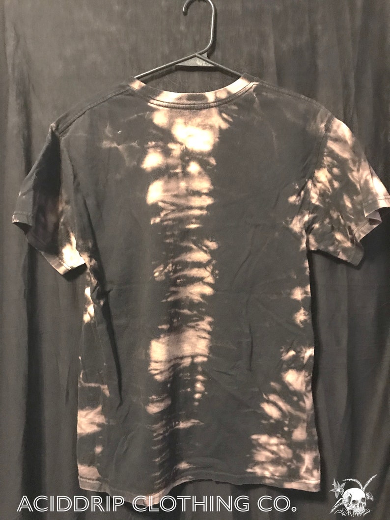 Puede incluir: Camiseta negra con un dise&ntilde;o salpicado de lej&iacute;a. La camiseta tiene cuello redondo y mangas cortas. El texto "ACIDDRIP CLOTHING CO." est&aacute; impreso en la parte inferior de la camiseta.