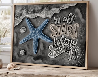 May include: A framed art print featuring a blue starfish, seashells, and the text "Not all stars belong in the sky" on a dark gray background. The artwork is displayed on a rustic wooden table near a window.