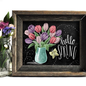 Puede incluir: Un cuadro enmarcado con una ilustraci&oacute;n de tulipanes rosas y morados en un jarr&oacute;n turquesa. Las palabras "hello SPRING" est&aacute;n escritas en blanco, con una mariposa amarilla. El marco es de madera r&uacute;stica.
