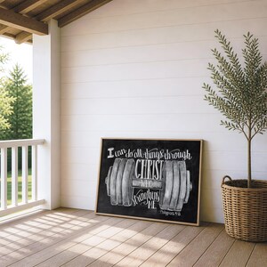 May include: A rectangular framed wall art piece featuring a black chalkboard-style background with a white illustration of a barbell. The text reads: I can do all things through CHRIST WHO strengthens ME - Philippians 4:13 in white script.