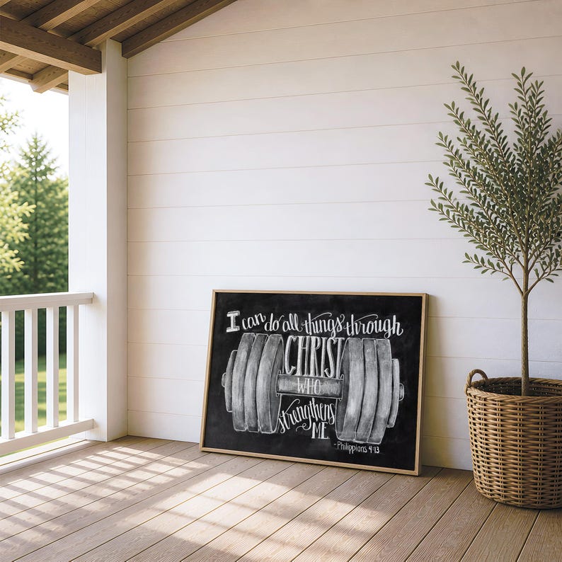 May include: A rectangular framed wall art piece featuring a black chalkboard-style background with a white illustration of a barbell. The text reads: I can do all things through CHRIST WHO strengthens ME - Philippians 4:13 in white script.