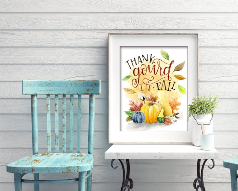 May include: A framed watercolor print with the text "Thank gourd it's fall" in a handwritten font. The print features a yellow gourd, a blue gourd, and a small green gourd surrounded by fall leaves and cotton bolls.