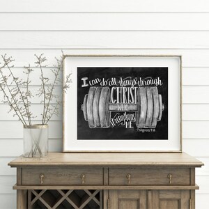May include: Framed black and white print featuring a barbell design with the text "I can do all things through Christ who strengthens me." The print is displayed on a wooden cabinet with a vase of dried flowers.