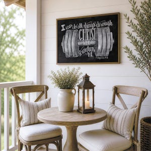 May include: A rectangular wall sign with a black background and a white chalk-style illustration of a barbell. The text reads: I can do all things through CHRIST WHO strengthens ME - Philippians 4:13. The sign is framed in a thin brown wood border.