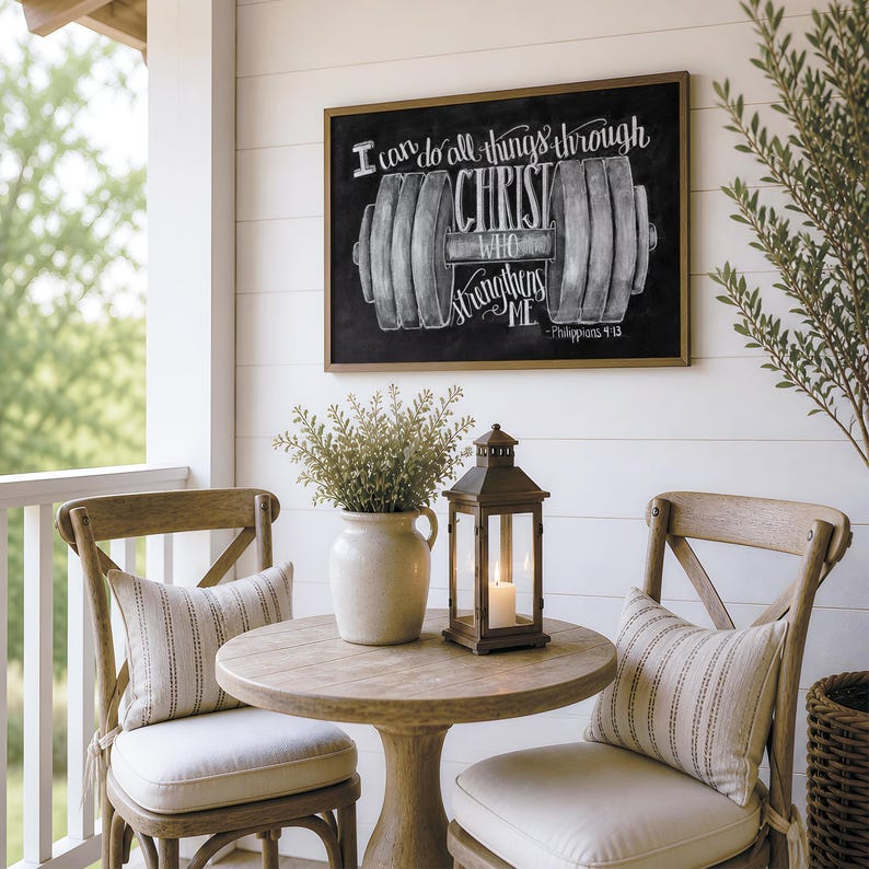 May include: A rectangular wall sign with a black background and a white chalk-style illustration of a barbell. The text reads: I can do all things through CHRIST WHO strengthens ME - Philippians 4:13. The sign is framed in a thin brown wood border.
