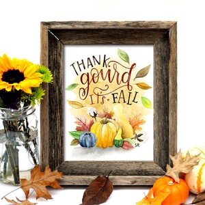 May include: A framed watercolor print with the text "Thank gourd it's fall" in red and brown lettering. The print features a watercolor illustration of gourds, pumpkins, and fall leaves on a yellow background.