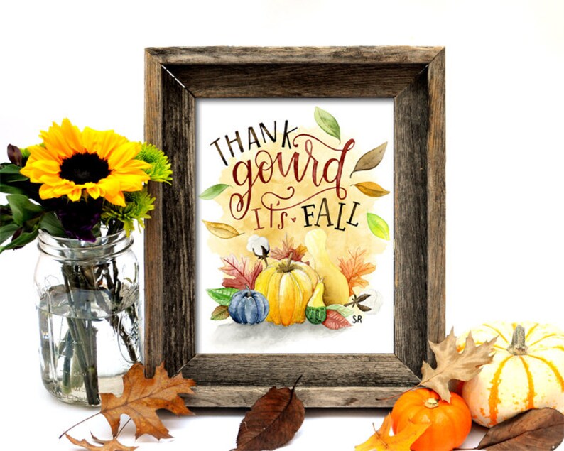 May include: A framed watercolor print with the text "Thank gourd it's fall" in red and brown lettering. The print features a watercolor illustration of gourds, pumpkins, and fall leaves on a yellow background.