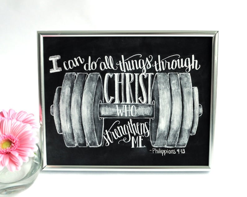 May include: Black framed chalkboard art with white lettering. The text reads "I can do all things through Christ who strengthens me - Philippians 4:13" with a barbell illustration. A pink flower is in the background.