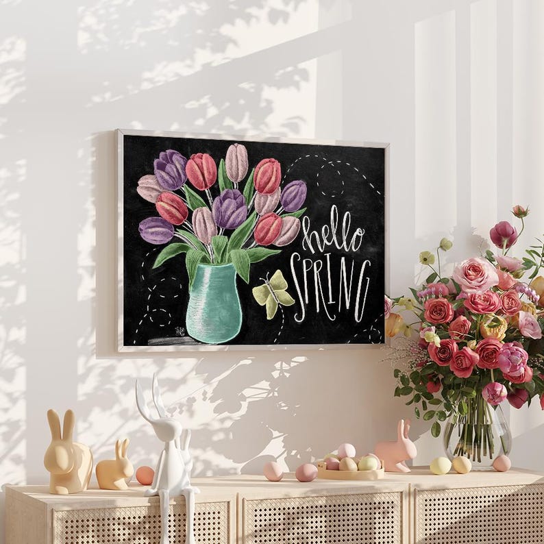 Puede incluir: Una obra de arte enmarcada presenta un ramo de tulipanes en un jarr&oacute;n turquesa sobre un fondo de pizarra negra. Las palabras "hello SPRING" est&aacute;n escritas en escritura blanca. Tambi&eacute;n se representa una mariposa amarilla. La obra de arte se exhibe en un mueble de color claro con decoraciones de Pascua.