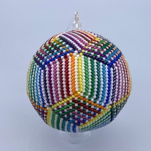 May include: A colourful beaded bauble with a rainbow pattern. The bauble is round and has a white background with stripes of red, orange, yellow, green, blue, indigo, and violet.