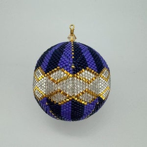 May include: A purple and blue beaded Christmas ornament with a gold and silver diamond pattern. The ornament is round and has a gold loop at the top.